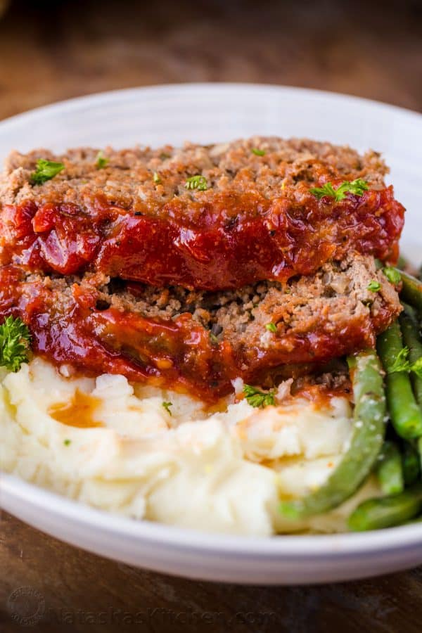 Meatloaf served on a plate with potatoes and greens and garnished with parsley