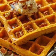 Pumpkin waffles stacked with whipped honey butter, toasted pecans, and maple syrup
