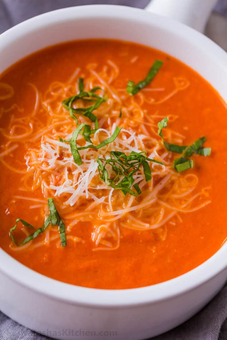 Bowl of creamy tomato soup garnished with parmesan and basil